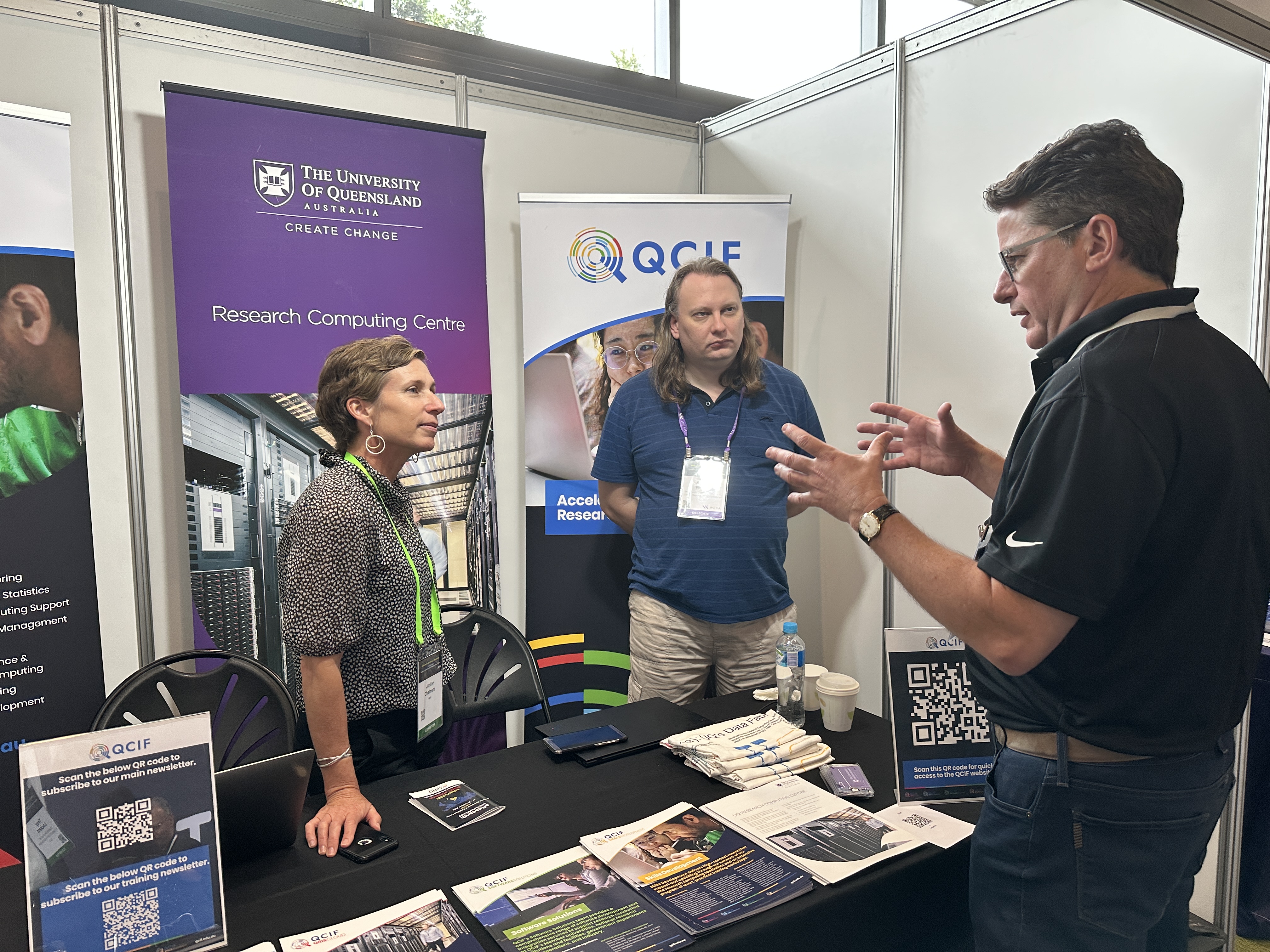 QCIF's Janine Chalmers and RCC's Ashley Wright talking with a conference attendee at the QCIF/RCC exhibition booth at eResearch Australasia 2022. (Photo: Troy Lockett.)